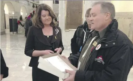  ?? JODIE SINNEMA/THE EDMONTON JOURNAL ?? Mike Dempsey, vice-president of the Alberta Union of Provincial Employees, passes a petition to Advanced Education Minister Lori Sigurdson. The almost 900 people who signed the petition are asking the province to keep Athabasca University headquarte­red...