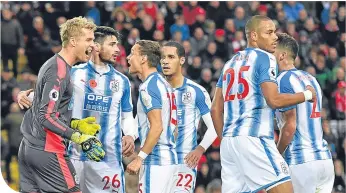  ??  ?? Jonas Lossl (left) is mobbed by his team-mates after saving Mohamed Salah’s penalty