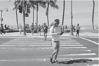  ?? AP Photo/Caleb Jones ?? A man uses his cellphone while crossing a street Wednesday in Honolulu. A new Honolulu ordinance allows police officers to issue tickets to pedestrian­s caught looking at a cellphone or electronic device while crossing a city street.