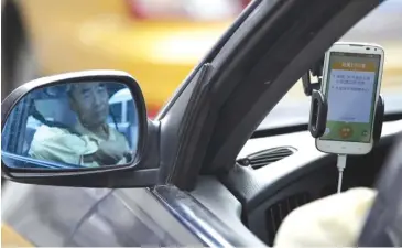  ?? REUTERS ?? A taxi driver is reflected in a side mirror as he uses the Didi Chuxing car-hailing applicatio­n in Beijing.