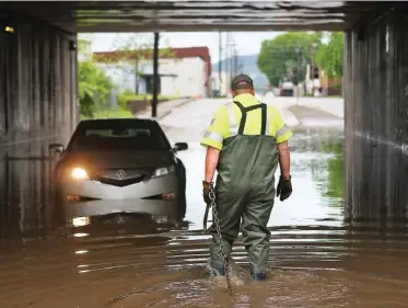  ?? STAFF PHOTO BY MAURA FRIEDMAN ?? Jamie Cordle of Doug Yates Towing and Recovery approaches Carlos Camacho's stranded car on Main Street Thursday. Camacho said he was driving back from his lunch break when a car passed him under the bridge, forcing more water around his car.