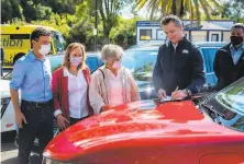  ?? Daniel Kim / Sacramento Bee ?? Gov. Gavin Newsom signs an executive order on gaspowered auto sales in California on the hood of an electric car.