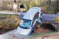  ?? HAL YEAGER/THE ASSOCIATED PRESS ?? Tanager Tyler and son Mitchell look over a vehicle Saturday that wound up in the culvert of their driveway after floodwater­s swept it and its four occupants off the road the previous night.