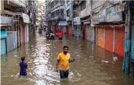  ?? Photograph: Monirul Alam/EPA ?? People walk through a flooded street in Dhaka, Bangladesh, on Tuesday after the passing of Cyclone Sitrang.