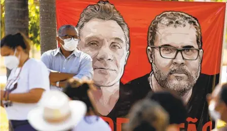  ?? ERALDO PERES AP ?? Workers of the National Indian Foundation, FUNAI, stand next to a banner with images of missing Indigenous expert Bruno Pereira (right) and freelance British journalist Dom Phillips, during a vigil in Brasilia, Brazil, on Monday.