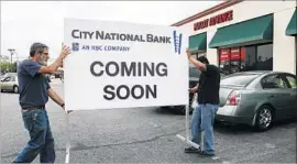  ?? Mark Boster Los Angeles Times ?? WORKERS CARRY a sign announcing the soon-to-be-opened City National Bank branch in a strip mall in the 3700 block of South Crenshaw Boulevard.