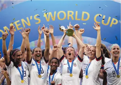  ?? ALESSANDRA TARANTINO/ASSOCIATED PRESS ?? Megan Rapinoe, middle, lifts up the trophy after the U.S. defeated the Netherland­s in the Women’s World Cup final on July 7, 2019. The U.S. Soccer Federation reached milestone agreements to pay its men’s and women’s teams equally.