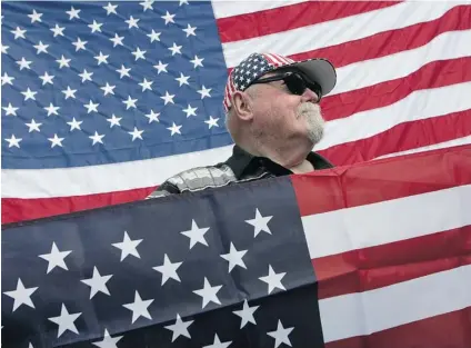  ?? JUSTIN SULLIVAN/ GETTY IMAGES ?? Al Kappdahl holds an American flag at a hillside with wooden crosses — a site honouring U. S. troops killed in Iraq — in Lafayette, Calif., in 2007. Pollster Michael Adams says Americans have a strong sense of patriotism and conformism.