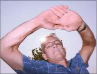  ?? GARY NYLANDER/The Daily Courier ?? Optometris­t Paul Clark holds his hands up to create a pinhole camera to project the image of the sun onto the ground without looking up. Clark is warning people not to look at next Monday’s solar eclipse, as doing so can cause total blindness.