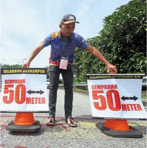  ?? ?? Mind the gap: an election worker placing signages reminding voters to keep a safe distance from one another to protect from Covid-19 infections at the polling centre in SMK Puncak Jalil, Seri Kembangan., Selangor. — azhar mahfof/the Star