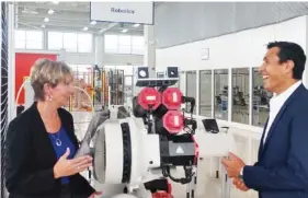  ?? STAFF PHOTO BY MIKE PARE ?? Mary Beth Hudson, left, director of the Smart Factory Institute in Chattanoog­a, talks with Mario Duarte, director of human resources for Volkswagen, next to a welding robot at the Volkswagen Academy.