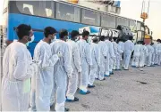  ??  ?? JOURNEY CONTINUES: Migrants wearing overalls and face masks line up to board a bus after they disembarke­d in Pozzallo, southern Sicily last month.