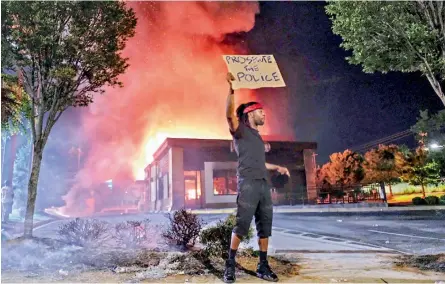  ??  ?? A person holds a sign as a Wendy’s restaurant burns on Saturday in Atlanta after demonstrat­ors allegedly set it on fire. Demonstrat­ors were protesting the death of Rayshard Brooks, a black man who was shot and killed by Atlanta police Friday evening following a struggle in the Wendys drive-thru line.
— AP/PTI