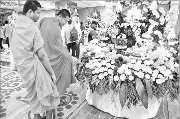  ??  ?? (Left) A worker sprays water on an elaborate fruit and vegetable decoration adorned with the photograph of Thailand’s Queen Sirikit. • (Right) Two Buddhist monks look at an elaborate display of carved fruits and vegetables during a fruit and vegetable...