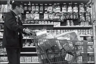  ?? ASSOCIATED PRESS ?? A MAN PUSHES A SHOPPING CART PAST A DISPLAY OF NUTS imported from the United States and other countries at a supermarke­t in Beijing on Monday. China raised import duties on a $3 billion list of U.S. pork, fruit and other products Monday in an...