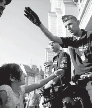  ?? AP/ SZILARD KOSZTICSAK ?? A migrant girl offers a flower to a police officer during a demonstrat­ion Tuesday outside a closed railway station in Budapest, Hungary, after migrants were not allowed to board trains bound for Germany because authoritie­s say they don’t have valid...