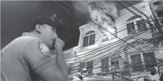  ??  ?? FIRE – A policeman covers his nose as firemen extinguish the blaze in a commercial building at Quintin Paredes in Binondo, Manila, Thursday night. Authoritie­s said the fire, which started from electrical faulty, caused a total of P1million worth of...