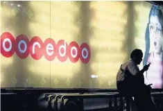  ??  ?? A man uses a mobile phone as he sits at a bus stop displaying advertisin­g for the Ooredoo telecom company, in Yangon, Myanmar.