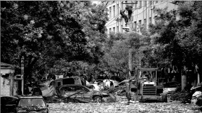  ?? PENG ZIYANG / FOR CHINA DAILY ?? Workers fix electrical cables as a bulldozer cleans garbage on the street in Suide county, Shaanxi province, on Thursday. A rain-triggered flood on Wednesday has left four people dead in the county.