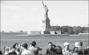  ?? AP/JOHN MINCHILLO ?? Tourists pass by the Statue of Liberty on Saturday in a boat that circles landmarks in New York. The statue will reopen to the public today after being closed by the federal government shutdown.