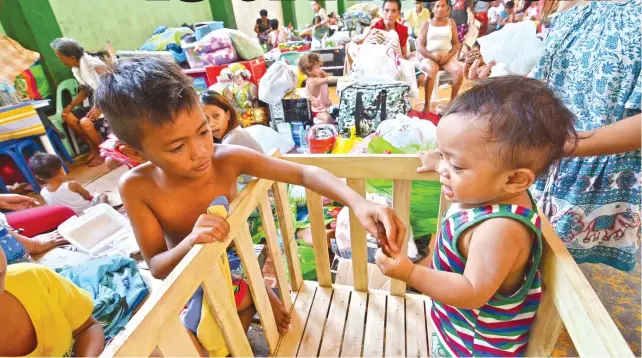  ?? SUNSTAR FOTO/ARNI ACLAO ?? TEMPORARY SHELTER. Children who are among some 2,500 persons left homeless by last Monday’s fire in Barangay Ermita, Cebu City play and share a snack in the sports complex that serves as their temporary home.