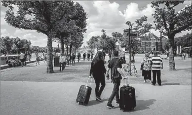  ??  ?? Toeristen met rolkoffers op het Museumplei­n in Amsterdam. (NRC)