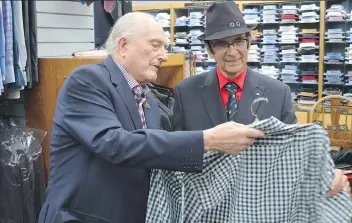  ??  ?? Frank Atchison, left, shows a shirt to customer Ed Ross at his clothing store. Atchison is planning to retire and close down the store after 46 years in business.
