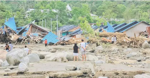  ??  ?? People stand as they look at damaged houses after a flash flood in Sentani, Papua, Indonesia. — Reuters photos