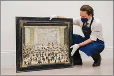  ?? (AP) ?? A member of staff holds ‘The Auction’, the only known painting of an auction room by the British artist L.S. Lowry, at Sotheby’s, in London, Tuesday, Oct. 19. The Auction will go under the hammer in London on Nov. 23 with an estimate of £1.2-1.8 Million.