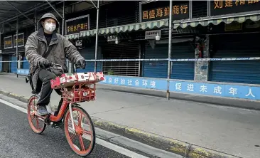  ?? GETTY IMAGES ?? A man rides past Wuhan’s closed Huanan Seafood Market on January 17.