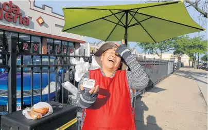  ?? ANTONIO PEREZ/CHICAGO TRIBUNE ?? Street vendor Carmen Nava laughs while showing off her licensed badge while selling tamales on June 19 in the 4300 block of West Armitage Avenue in Chicago. Nava said that getting the license was difficult, time-consuming and expensive.