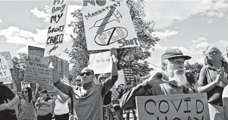  ?? NANCY LANE/BOSTON HERALD ?? Protesters hold signs Aug. 30 at the Massachuse­tts State House. Medical staffs say efforts to treat COVID-19 are complicate­d due to politics.