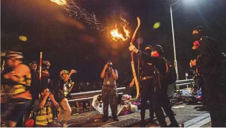  ?? — aFP ?? Taking aim: Protesters watching as a fire arrow is released to light a barricade outside CuhK.