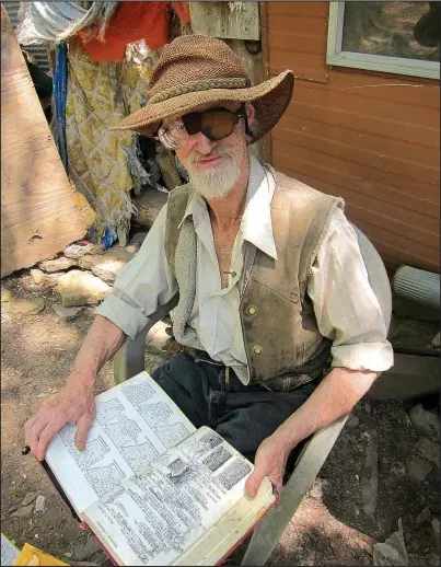  ?? Photo courtesy Kelly Mulhollan ?? Kent Bonar lives in rural Newton County with a passel of dogs and cats, a well for water, a solar charger for his radio and his passion for the outdoors. In his lap is the book on Arkansas flora he illustrate­d over the course of some 30 years.