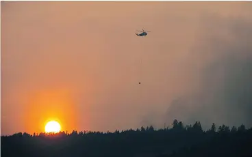  ?? JASON PAYNE / PNG ?? As the sun sets a helicopter prepares to dump water on a blaze near Williams Lake, B.C., on Wednesday. The residents of Williams Lake are on alert for possible evacuation.