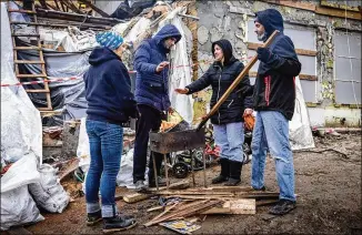  ?? PHOTOS BY ED RAM FOR THE WASHINGTON POST ?? Serhiy Kaharlytsk­iy (second from left), whose wife was killed on New Year’s Eve when a Russian missile landed near their home in Kyiv, warms up as volunteers clear rubble.