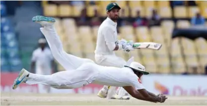  ??  ?? COLOMBO: Sri Lankan cricketer Dimuth Karunaratn­e (L) dives for the ball as Zimbabwe cricketer Sikandar Raza looks on during the third day of a one-off Test match between Sri Lanka and Zimbabwe at the R Premadasa Cricket Stadium in Colombo yesterday. —...