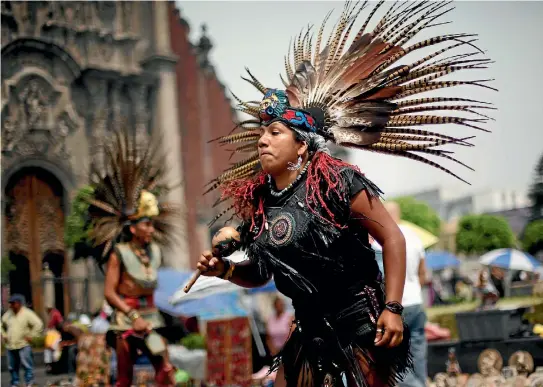  ??  ?? A group performs an Aztec dance for tourists outside the Metropolit­an Cathedral in Mexico City.