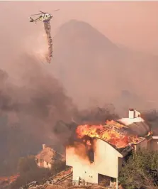  ?? RINGO H.W. CHIU/AP ?? A helicopter drops water as a wildfire burns a home near Malibu Lake in Malibu, California, on Friday. All 13,000 residents of Malibu were ordered to evacuate Friday.