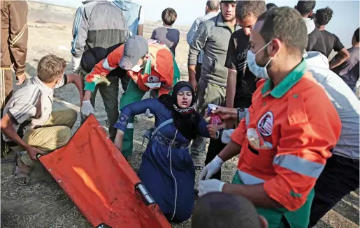  ?? AP ?? Palestinia­n medics help a woman who fainted from teargas fired by Israeli troops during a protest at the Gaza Strip’s border with Israel on Tuesday. —