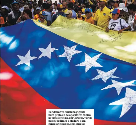  ??  ?? Bandeira venezuelan­a gigante num protesto de opositores contra as presidenci­ais, em Caracas. Vários países pediram a Maduro para cancelar eleições, sem sucesso