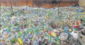  ??  ?? A woman sits among plastic bottles segregated for recycling.
PTI