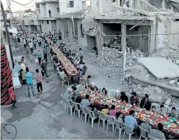  ?? HAMZA AL-ALWEH/GETTY IMAGES ?? Syrian residents of the rebel-held town of Douma, on the outskirts of the capital Damascus, break their fast on a heavily damaged street on Sunday, during the Muslim holy month of Ramadan.