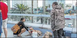  ?? L.E. Baskow Las Vegas Review-journal ?? A woman stops to pet a dog with sunglasses as panhandler­s and performers occupy spots along the pedestrian bridge leading to New York-new York.