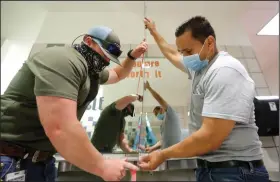  ?? (AP/LM Otero) ?? Matt Attaway (left) and Rogelio Ponciano of the Richardson Independen­t School District in Dallas install a plexiglass barrier Wednesday on a sink in a student restroom at Bukhair Elementary School.