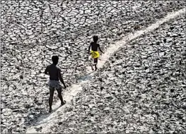  ?? MANISH SWARUP / AP ?? A man and a boy walk across an almost dried up bed of river Yamuna following hot weather in New Delhi, India on Monday. An unusually early and brutal heat wave is scorching parts of India, where acute power shortages are affecting millions as demand for electricit­y surges to record levels.