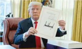  ?? | AP ?? President Trump shows off the tax bill after signing it in the Oval Office Friday.