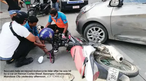  ?? JOY TORREJOS ?? Rescuers help an injured motorcycle rider after he was hit by a car on Hernan Cortes Street, Barangay Cabancalan, Mandaue City yesterday afternoon.