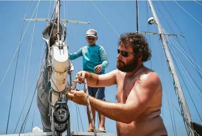  ?? Mark Mulligan / Staff photograph­er ?? Chris Huslage works with his son, Jonathan, 11, to secure their sailboat’s main sail as the family readies for tropical weather.