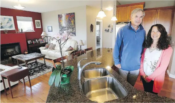  ??  ?? Chris Nation and partner Betty Gnocato in the kitchen, which has a granite-topped counter. To the left, a dramatic brick-red wall in the family room is accented by white walls and white leather sofas. The coffee table has an acid-etched metal top and was made by artist Bernhard Rohne. The painting of a rushing forest river was painted by Bi Yuan Cheng. “I love how his work combines the West Coast wilderness with a Chinese style,” says Chris. The two are keen kayakers in areas such as the Broken Group of islands and Clayquot Sound. The carpet was bought on a trip to Turkey in 2019 and cushions are from Thailand. Over the mantle is a painting by local artist Ann Hunter.